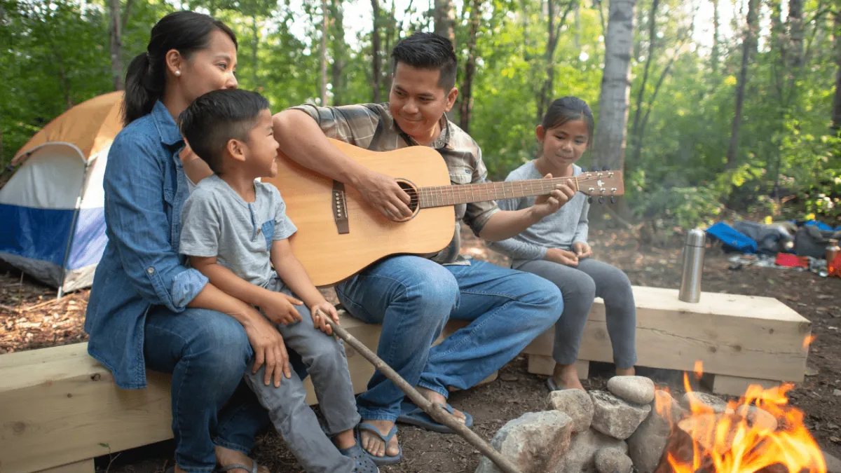 A happy student playing and singing around the campfire with his family