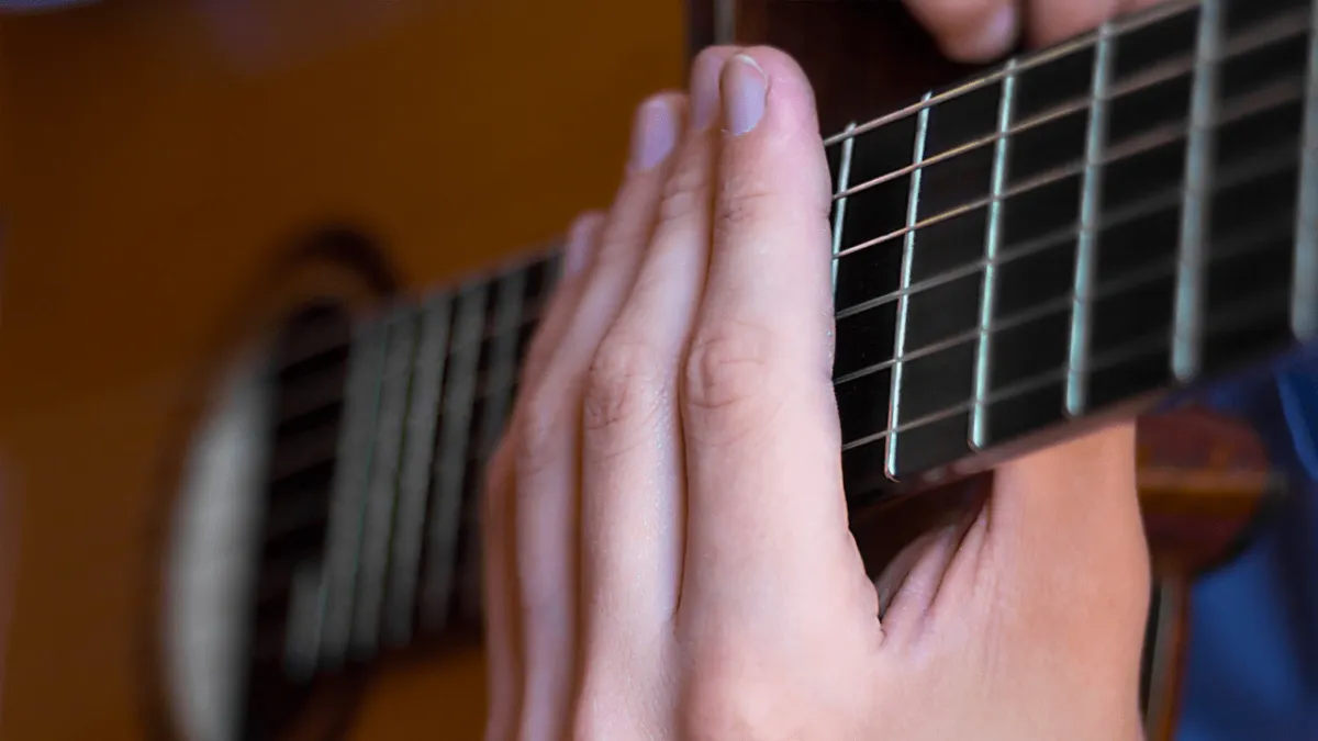 Guitarist placing fretting hand across all six strings to demonstrate muted strumming drill.
