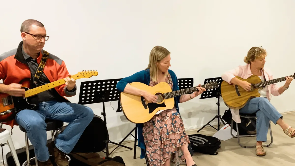 Three adults smiling during a free beginner guitar lesson on the Gold Coast