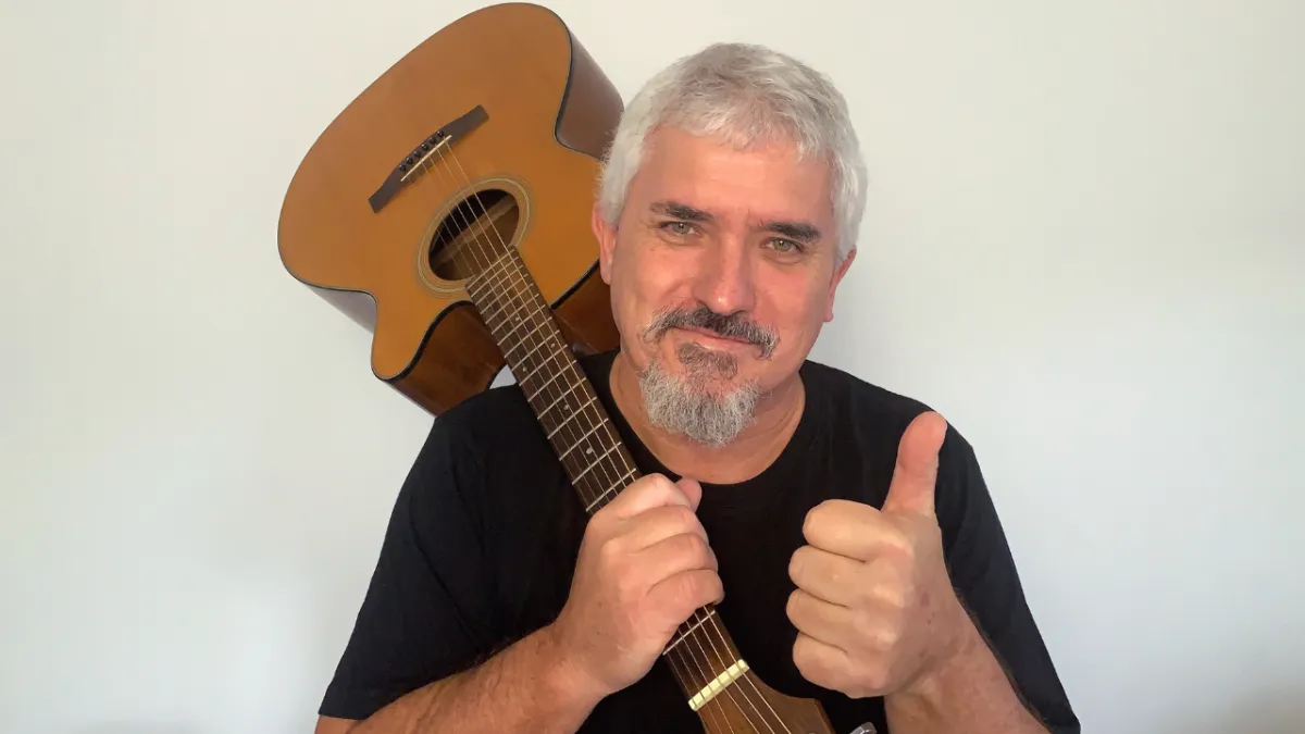 Allen Hopgood, smiling and holding an acoustic guitar, giving a thumbs up — representing the friendly, supportive approach at Gold Coast School of Guitar for adults over 40.
