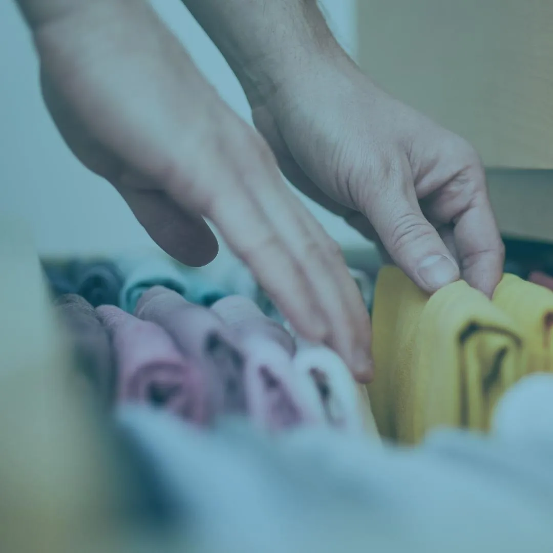 Hands neatly organizing folded clothes in a drawer, illustrating ADHD-friendly organizing strategies for professional organizers