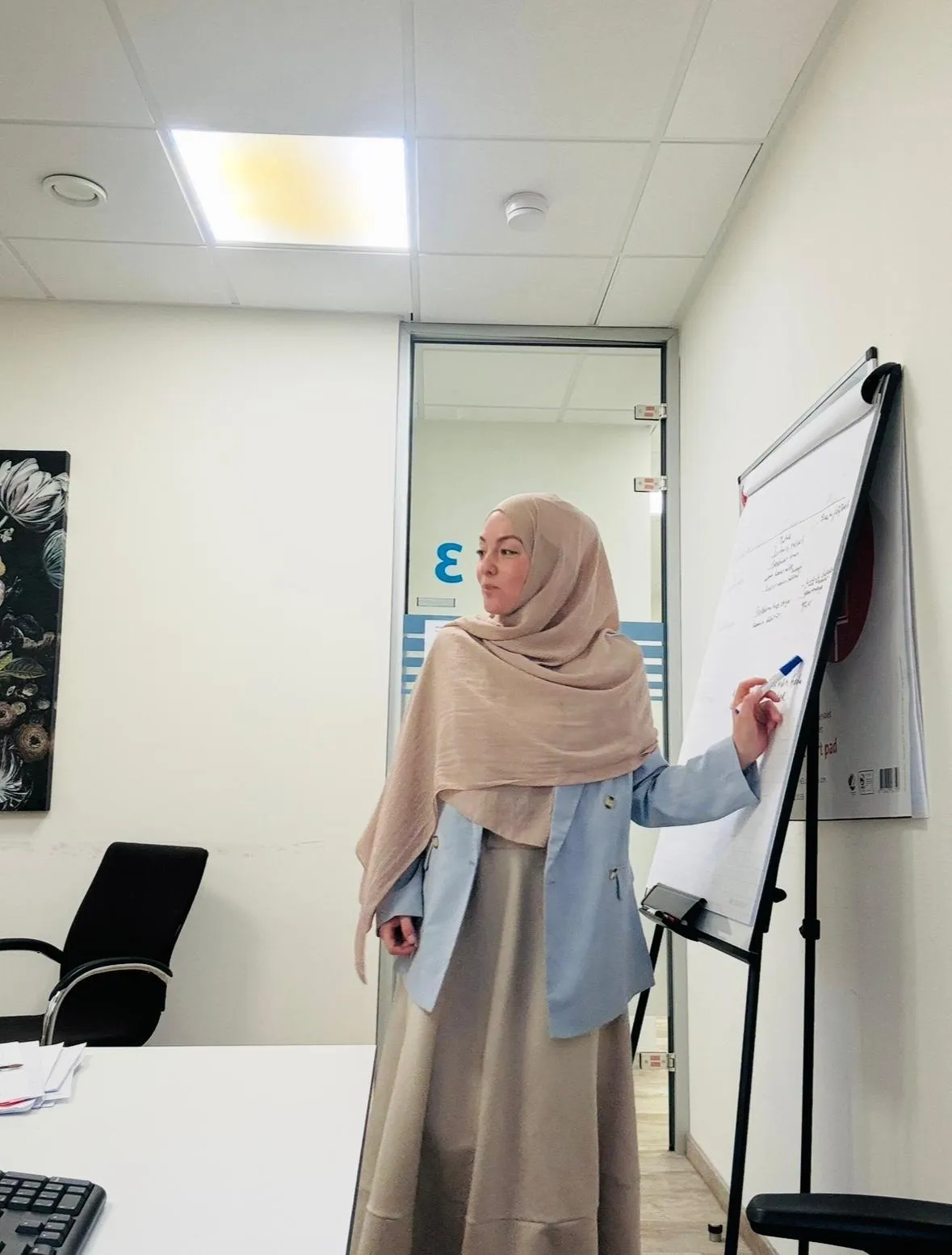 A Turkish woman in her 40s sits at a cozy desk with a laptop, a cup of tea, and a notepad, sunlight streaming through a window, soft feminine decor, calm and inviting atmosphere.