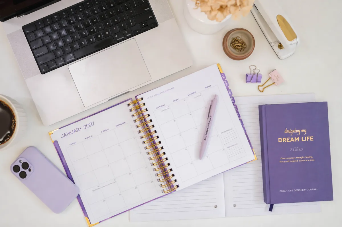 Flat lay of a pastel-colored planner open on a marble table with a cup of coffee and pens next to it