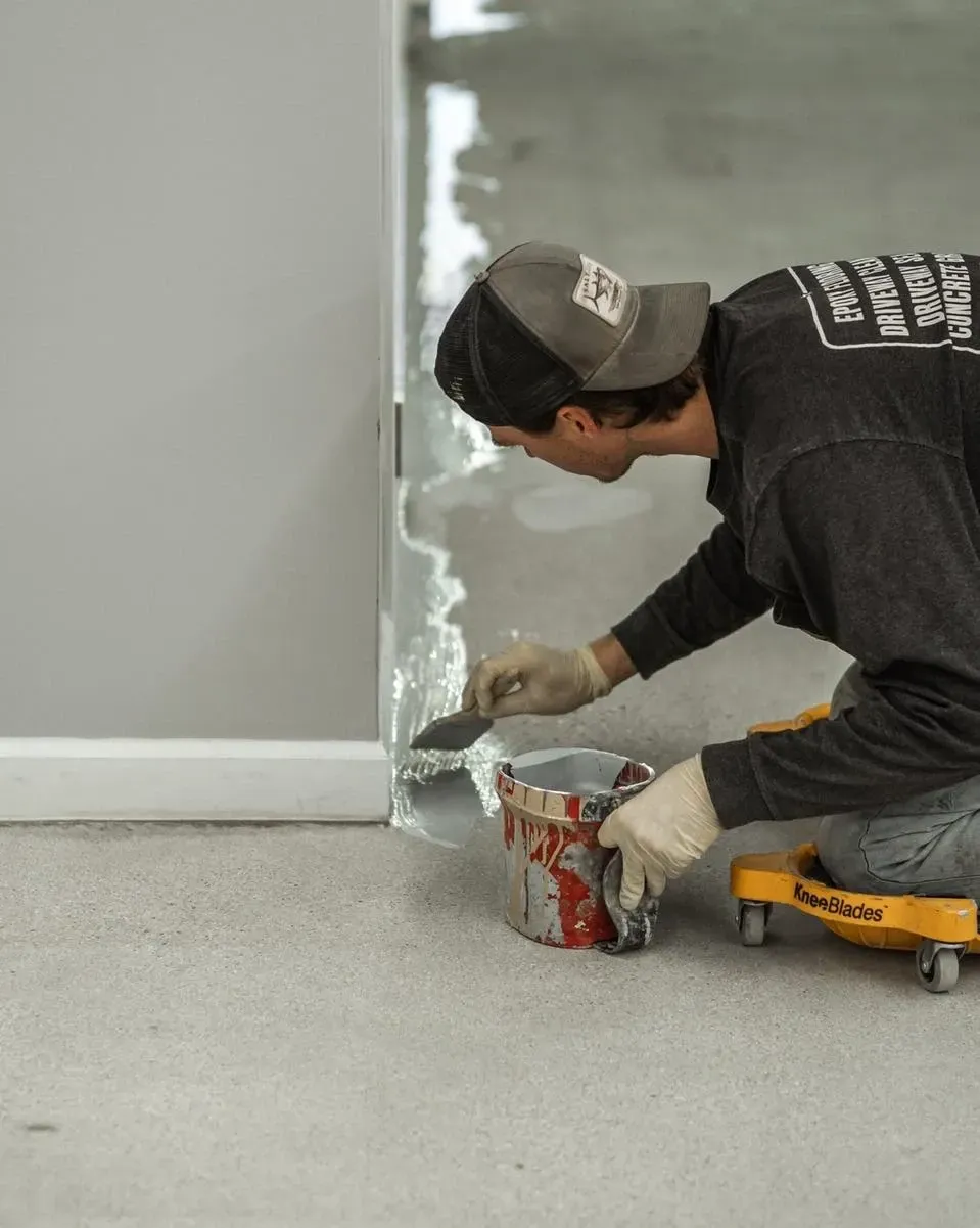 Professional installer applying epoxy coating along the edge of a concrete floor during garage floor preparation.