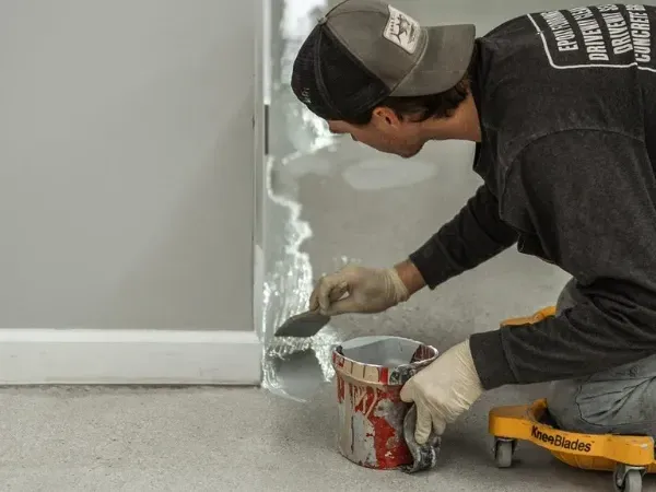 Professional installer applying epoxy floor coating along the edge of a concrete surface during the installation process.