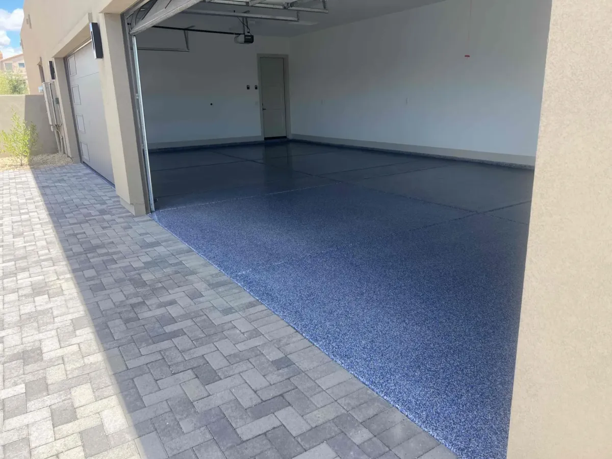 Open garage with a newly installed blue epoxy flake floor coating and paver driveway outside.