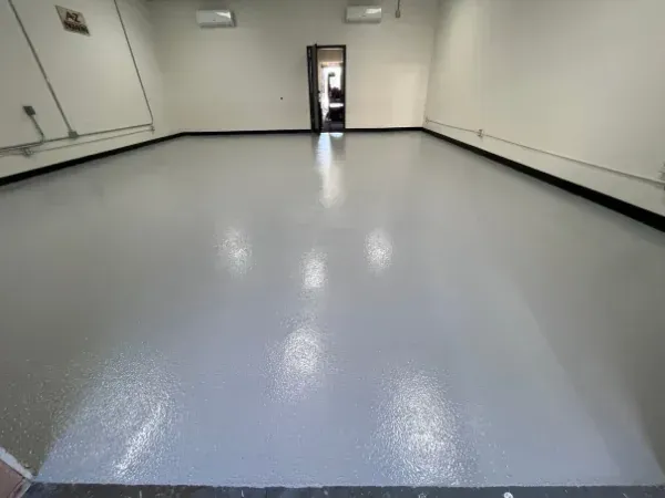 Fresh epoxy floor coating installation with smooth light gray finish in empty space