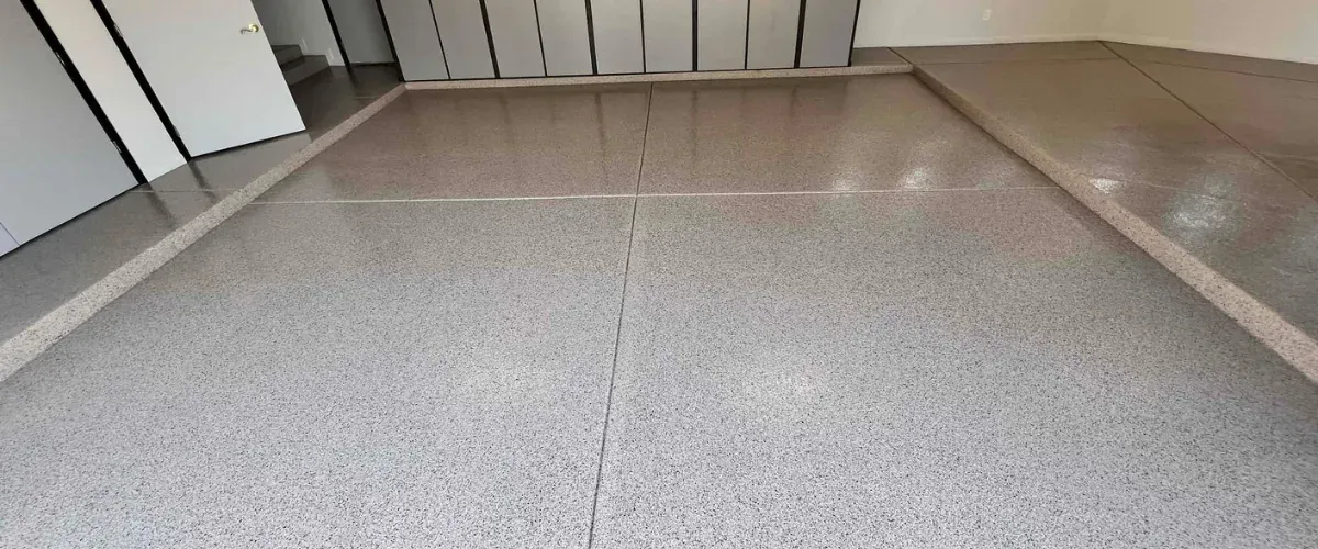 Finished epoxy garage floor with flake coating and full wall cabinet storage system in the background.