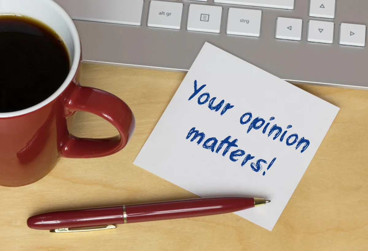 Coffee cup, pen keyboard and note saying Your Opinion Matters!