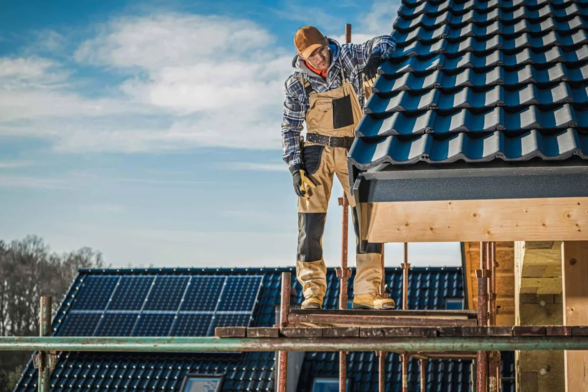 Roofing contractor inspecting new roof installation with solar panels in background, showcasing professional roofing services by Birch Roofing.