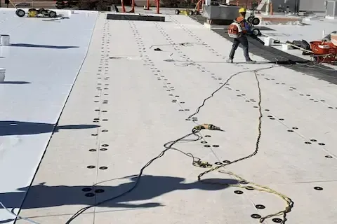 Roofer securing TPO membrane to flat commercial roof with safety harness in Woodbury