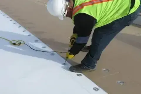Safety-geared technician mechanically fastening TPO membrane on flat commercial roof