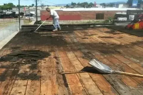 Roofer stripping old material from flat roof deck during commercial roof replacement