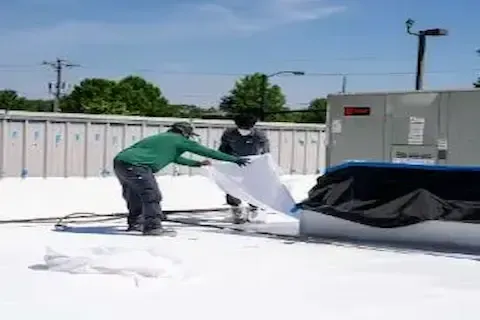 Two-man crew laying flat roofing membrane on commercial building in Woodbury