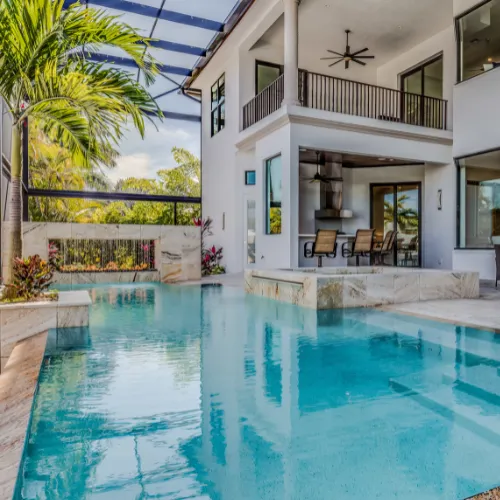 Screened-in backyard swimming pool beside a modern two-story home with a covered patio and palm tree