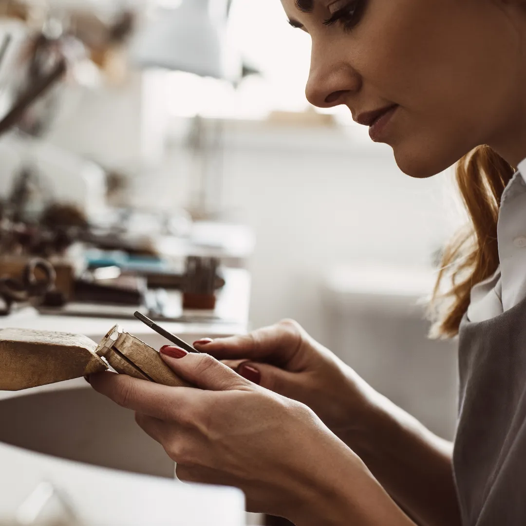 Fine artisan jeweler hand-shaping precious gold and silver metals in a sunlit atelier