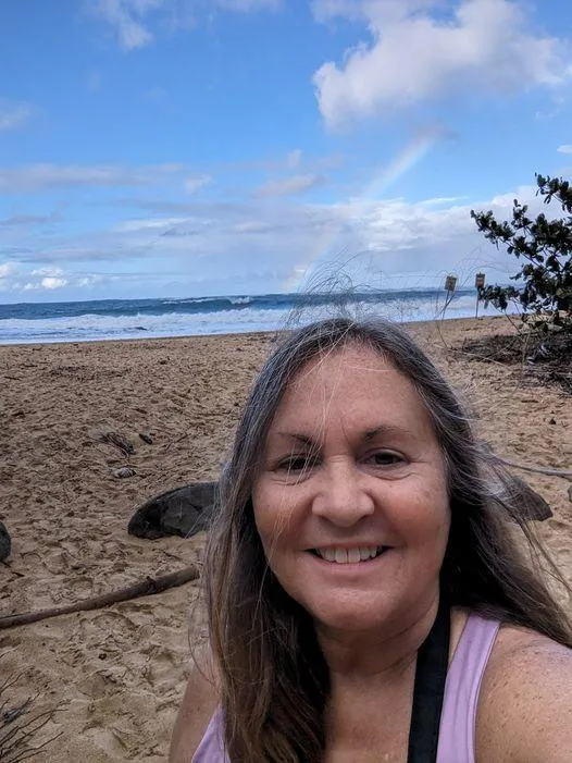 photo of a woman, Jodie, at the beach with a rainbow behind her