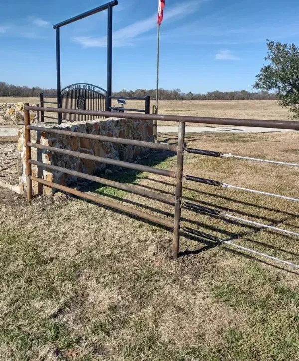 Metal ranch entry gate with tensioned cables and stone pillars