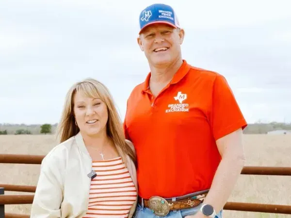Smiling man in a cowboy hat and yellow polo shirt standing in front of a corrugated metal wall