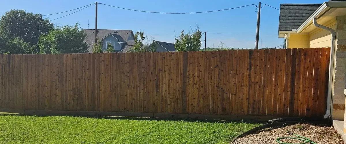 Wooden privacy fence enclosing a backyard with green grass and a sunny sky.