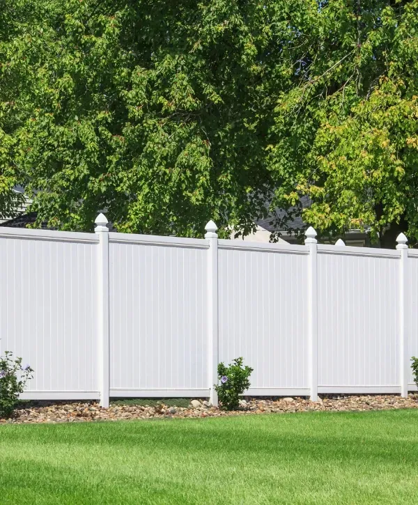 White vinyl privacy fence in a residential backyard with green grass and trees.