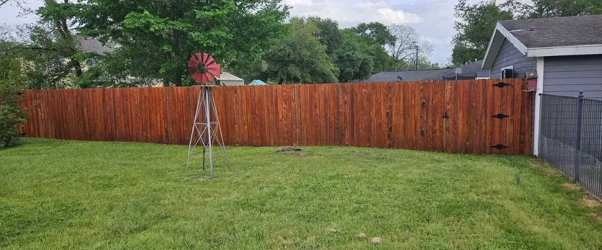 Freshly stained red-toned wooden backyard fence in a suburban yard