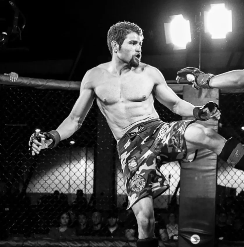 Paul Puleo, the owner of Fight Fit and a private martial arts instructor, is seen in an MMA ring, executing a powerful right kick on a training pad.