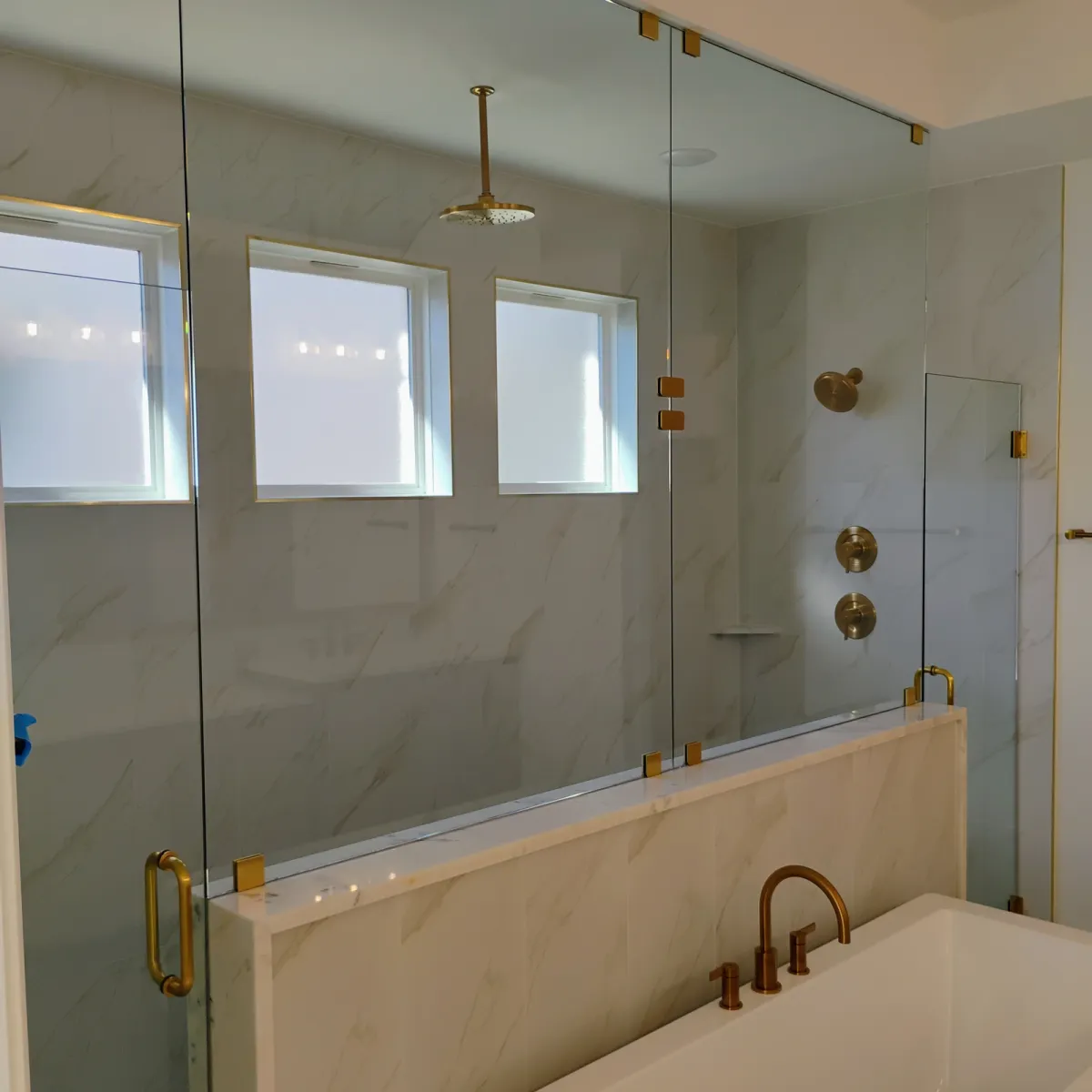 Frameless glass shower wall with brass fixtures beside a soaking tub