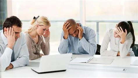 Four people at a desk looking dismayed.