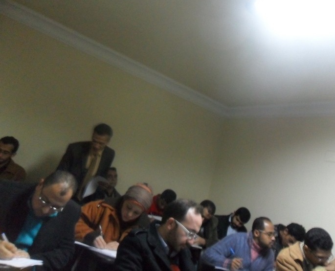 People sitting around a long conference table in a dimly lit room, focusing on a presentation.