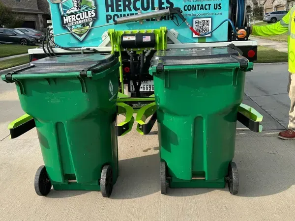 Two green trash bins positioned behind a Hercules cleaning truck for service