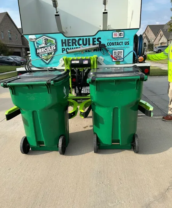Two green outdoor trash bins positioned on a trash can cleaning truck lift
