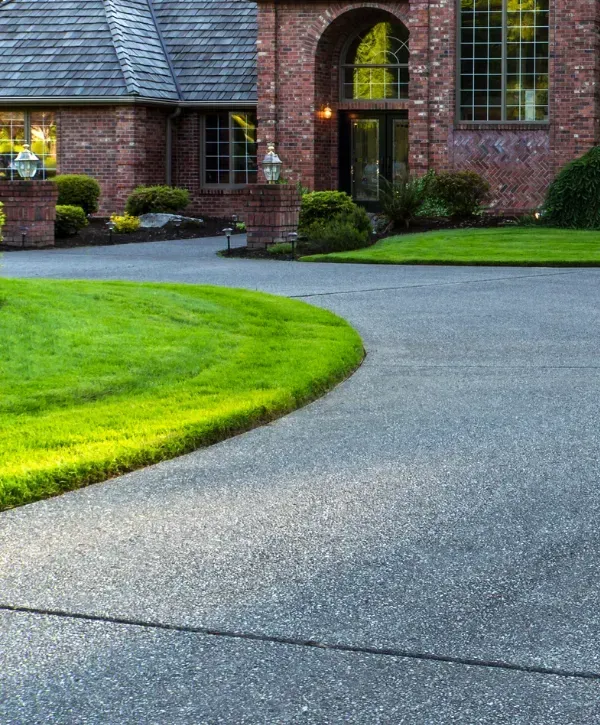 Curved concrete driveway leading to a large brick home with well-maintained landscaping