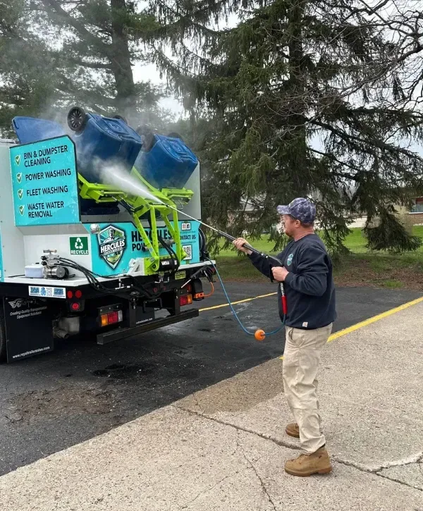 Technician pressure washing overturned trash bins mounted on cleaning truck