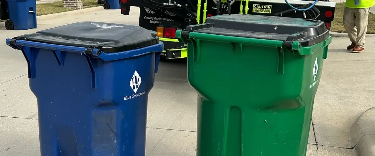 Blue recycling bin and green trash bin sitting at the curb in a residential neighborhood
