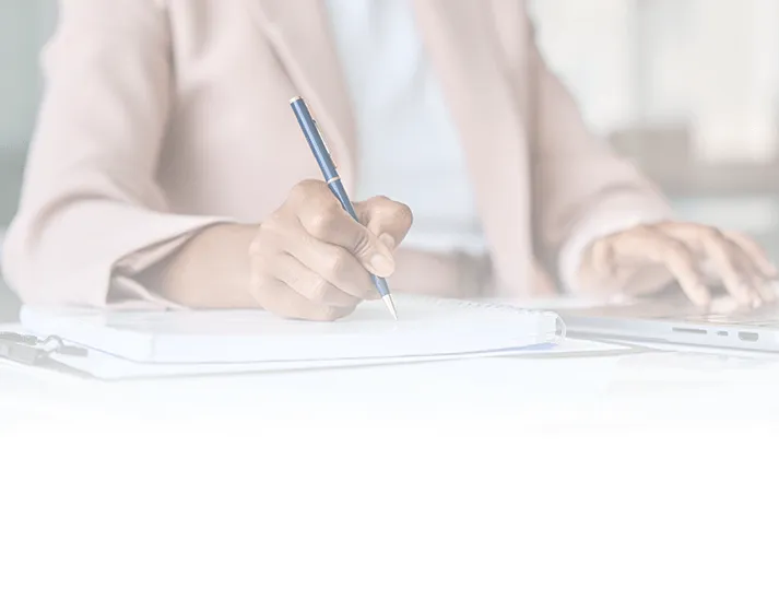 A professional woman taking notes in the Summit workbook while also working on a laptop, capturing strategies and actionable steps to succeed in real estate investing.