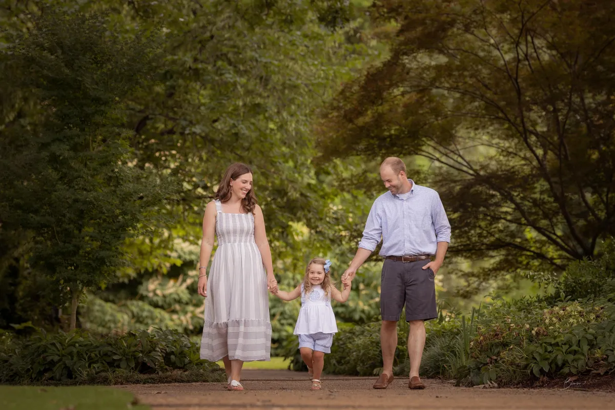Family of three walking hand in hand through a Raleigh park during fall session