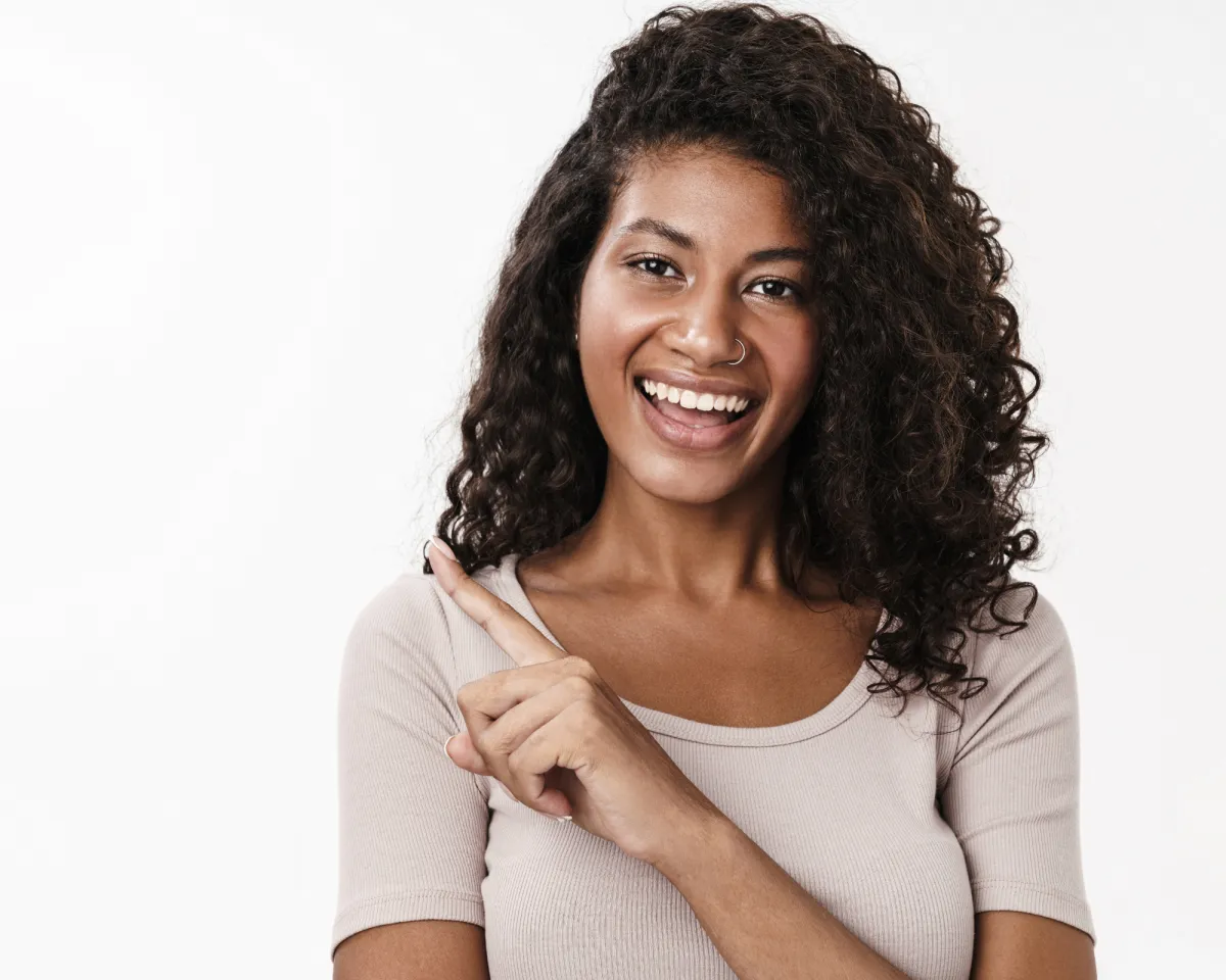 A confident young woman in business attire stands in a bright, modern office, holding a specimen collection kit and smiling, with a cityscape visible through large windows behind her.