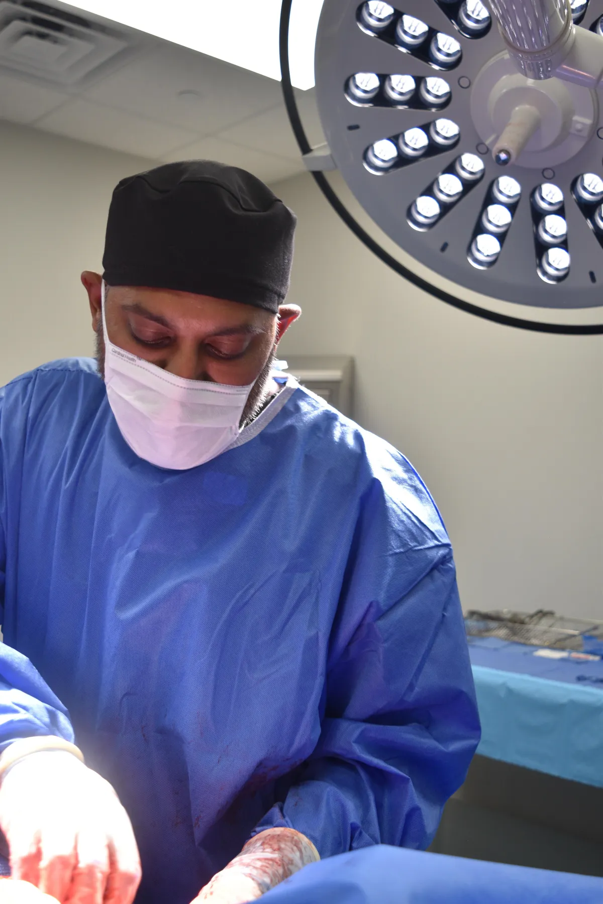 Dr. Shitel Patel, board-certified plastic surgeon at Lift Plastic Surgery in Houston, performing a precision cosmetic procedure in the operating room, dressed in blue surgical gowns.