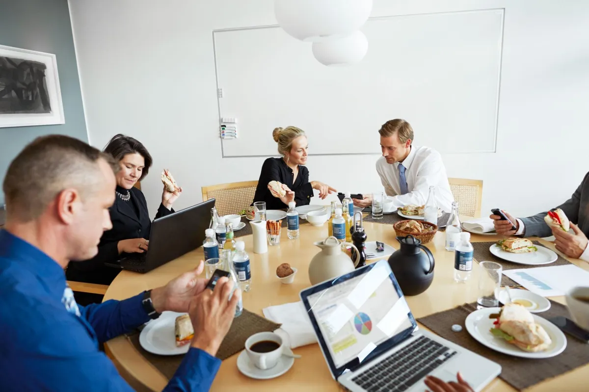 6 office workers itting around a table full of laptops and coffe cups, speaking to each other