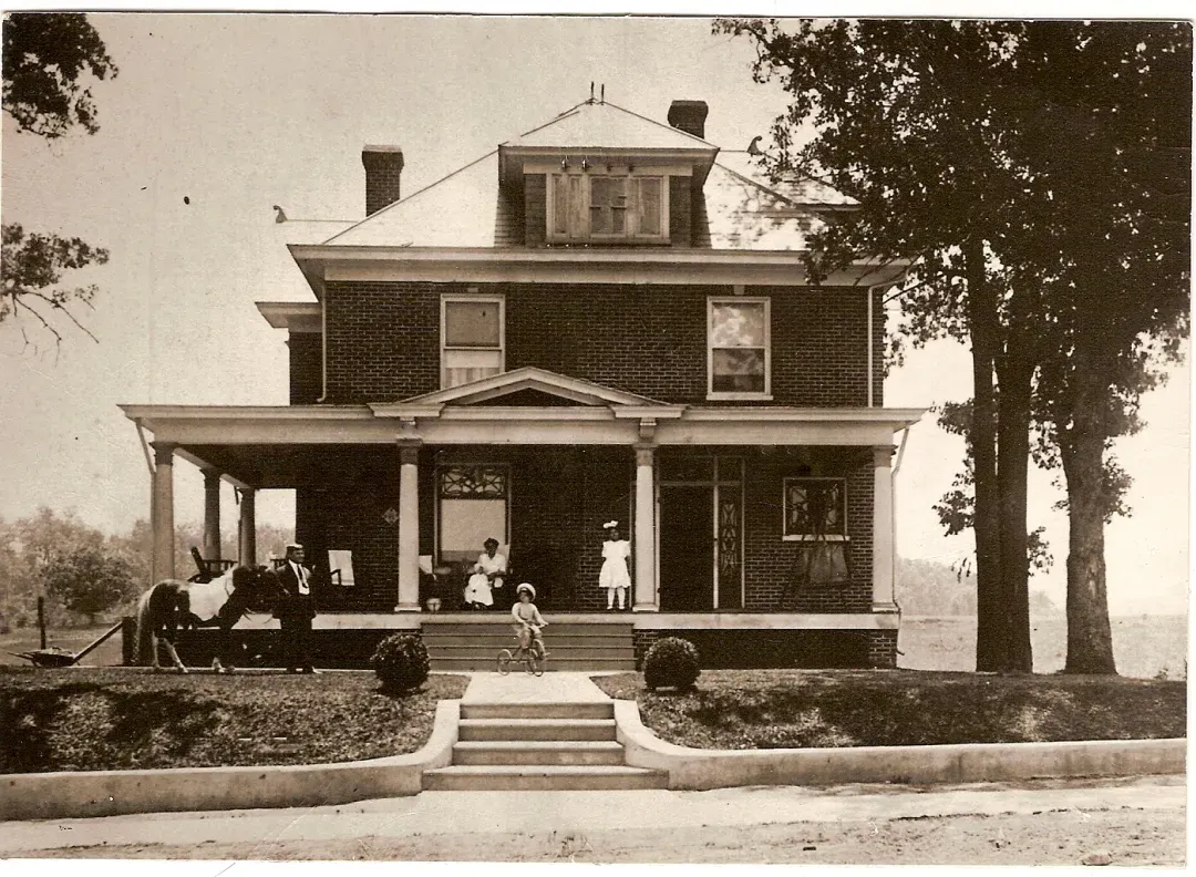 A Black and white photo of an African-American family and horses on the front porch a house for the 19th century