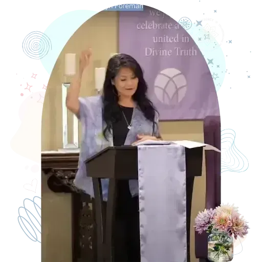 Women gesturing while standing at a podium in a room with spiritual banners