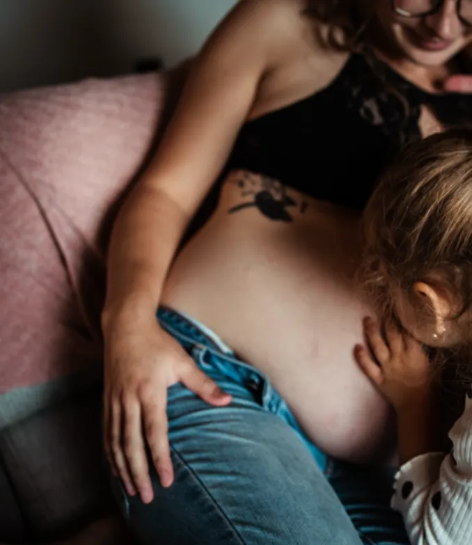 Image of a young girl, kissing her mother's pregnant belly. Image represents the top of page for MSP Doula, an inclusive and informed doula support service in the Twin Cities of Minneapolis and Saint Paul, Minnesota.