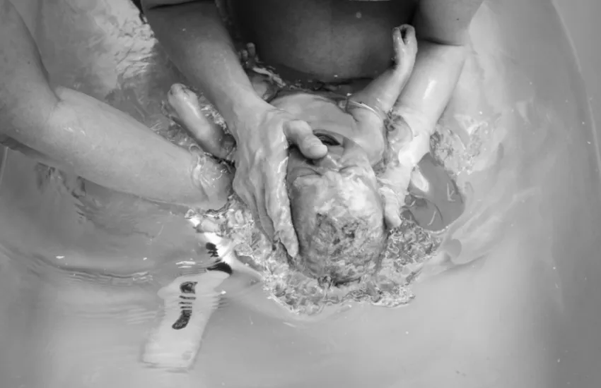 A baby being born in the water during a doula supported birth. Image to support testimonial from Jess in Minneapolis, Minnesota.