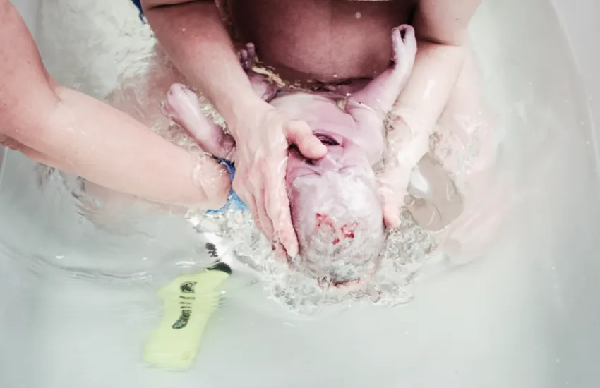 A baby being born in the water during a doula supported birth. Image to support testimonial from Jess in Minneapolis, Minnesota.