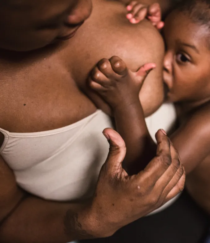 A Black mother breastfeeds her toddler child. 