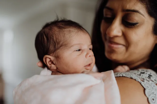 A new mom burps her baby at her shoulder after she is done breastfeeding