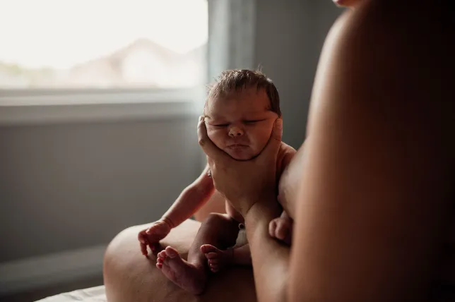A new mom holds her newborn on her knee to burp following breastfeeding