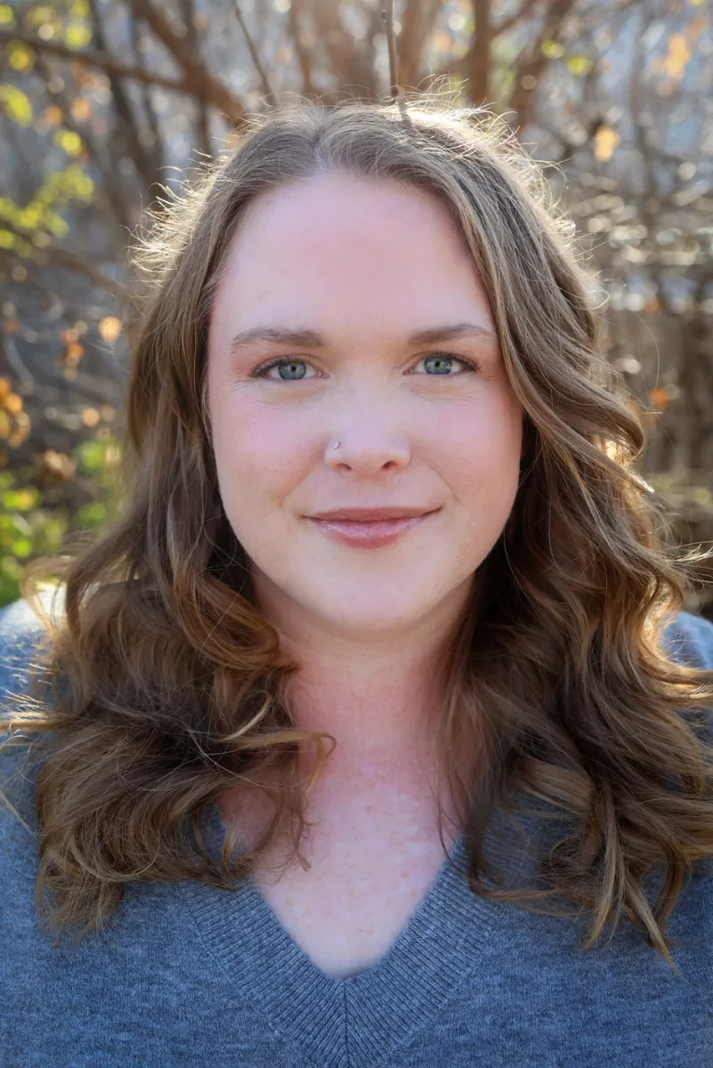 An image of Twin Cities doula, Jillian Carpenter, smiling at the camera while lounging on her blue couch in her Minneapolis, Minnesota home.