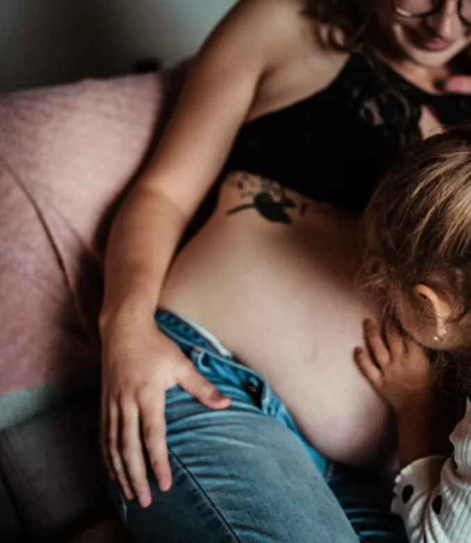 Mobile version of Image of a young girl, kissing her mother's pregnant belly. Image represents the top of page for MSP Doula, an inclusive and informed doula support service in the Twin Cities of Minneapolis and Saint Paul, Minnesota.